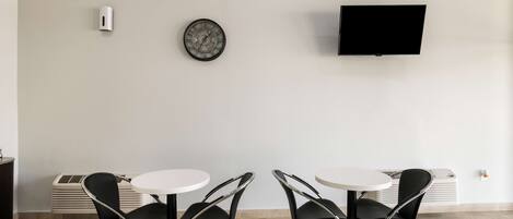 Een kamer met twee ronde tafels en vier zwarte stoelen, een flatscreen televisie aan de muur en een decoratief bord erboven.