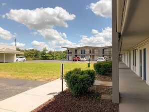 A motel with a covered parking area, a grassy lawn, and a row of rooms with a blue door.