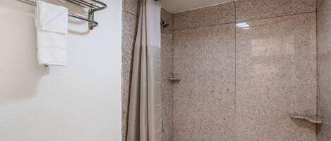 A bathroom with a shower, a towel rack with folded towels, and a bathtub.