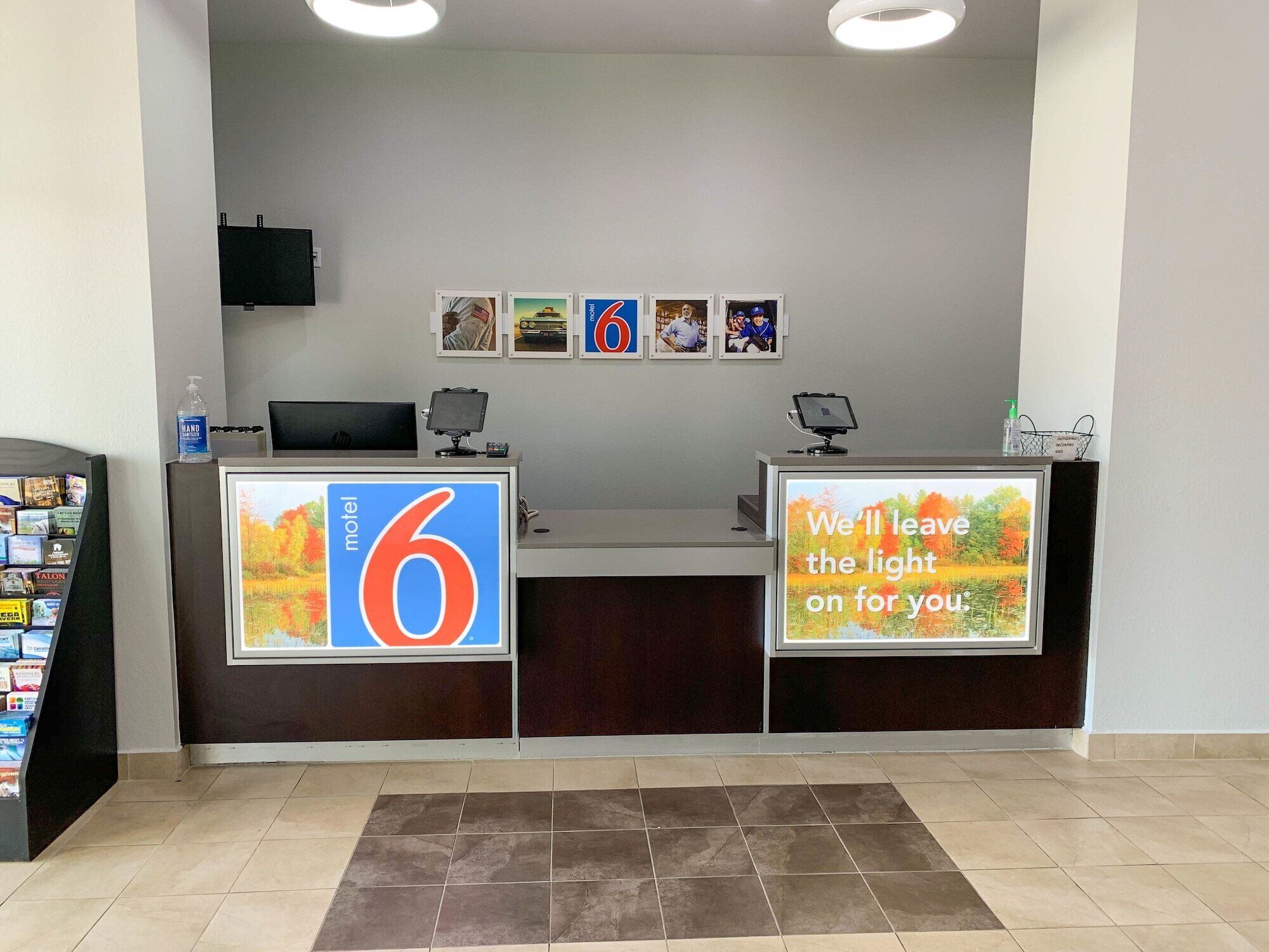 A hotel reception desk with a large '6' sign, a digital display with a message, and a series of framed pictures on the wall.