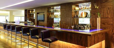 A modern bar area with wooden paneling, bar stools, and a variety of liquor bottles.