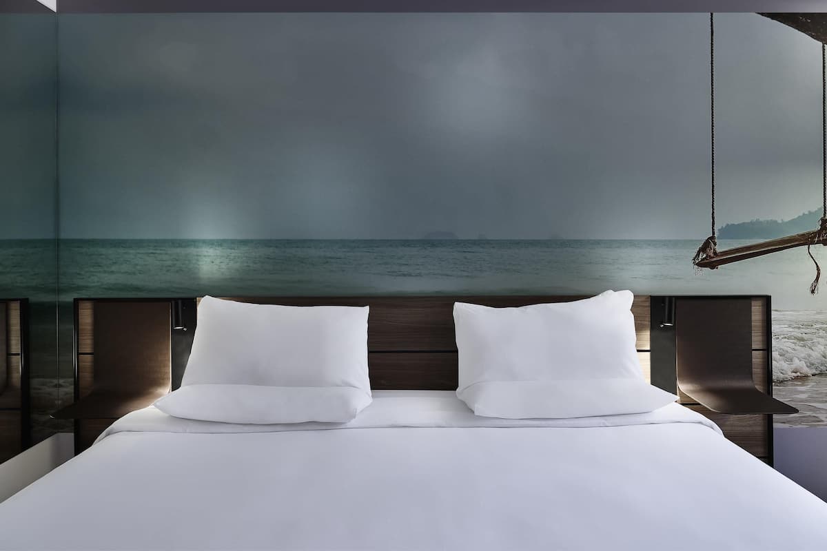 Un dormitorio con cama, dos almohadas, cabecera de madera y vista al mar a través de un ventanal amplio.