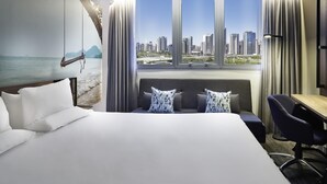 Een hotelkamer met een groot bed, een bureau en een uitzicht op een stadsbeeld door grote ramen.