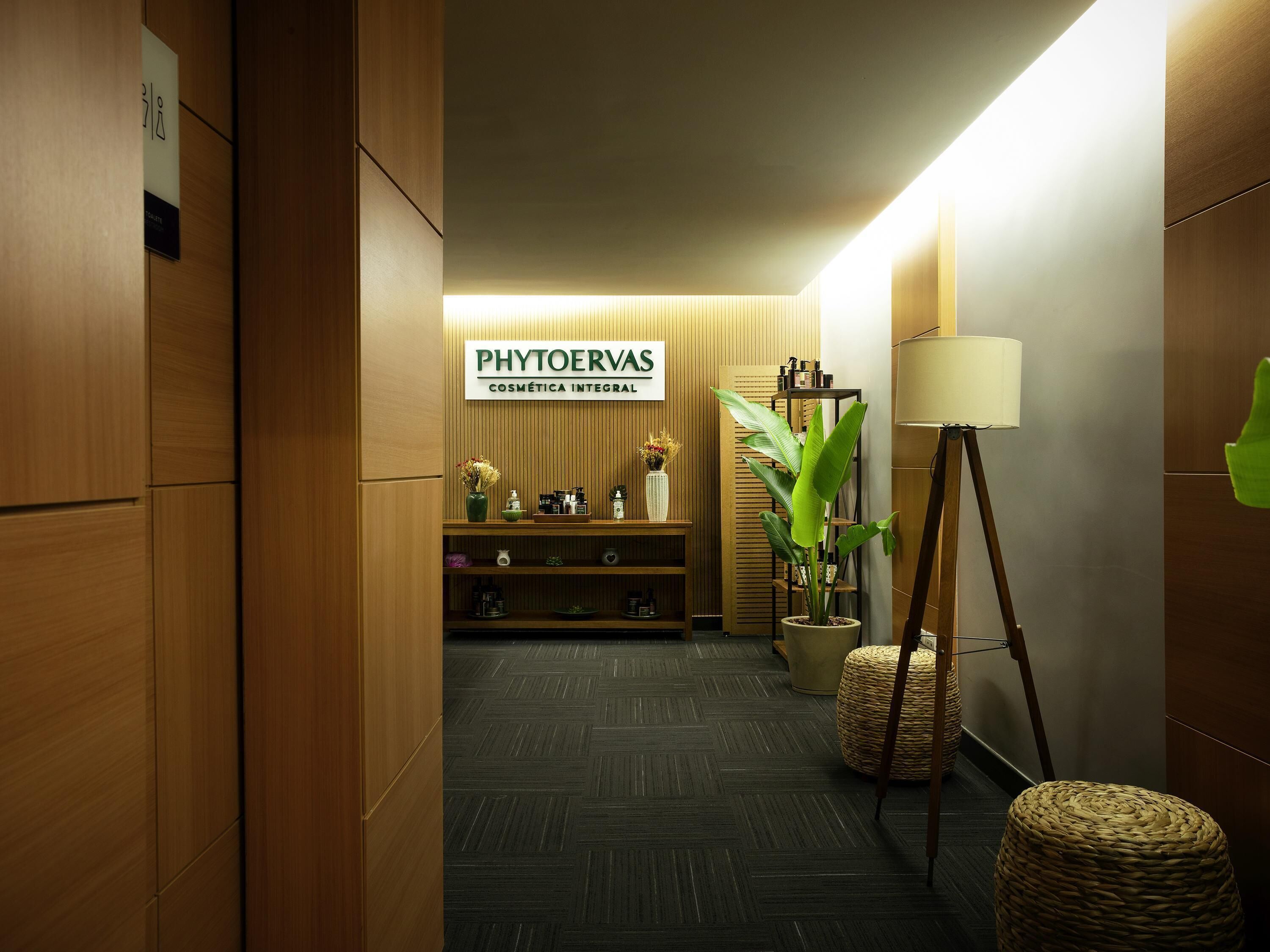 A hallway with wooden paneling, a sign for 'PHYTOERVAS COSMETICA INTEGRAL,' a potted plant, a lamp, and a woven stool.