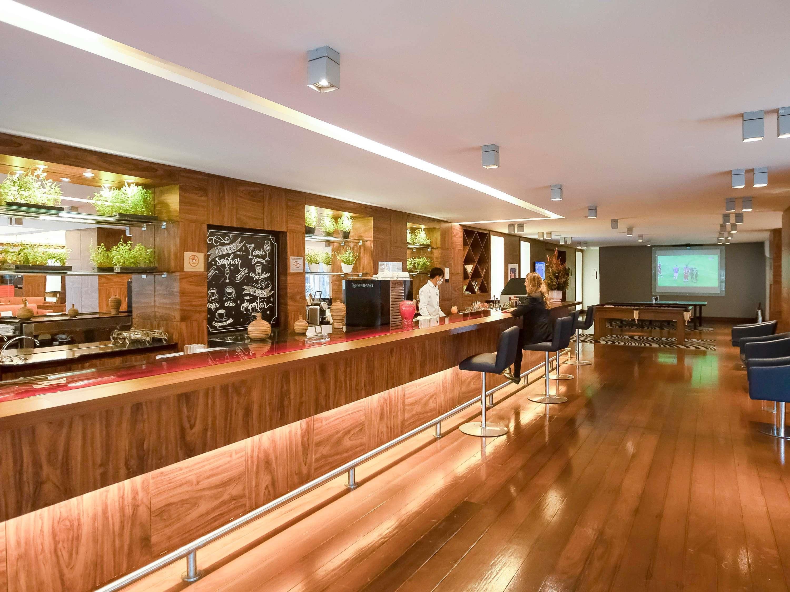 A bar area with a wooden counter, bar stools, a coffee machine, and a projection screen.