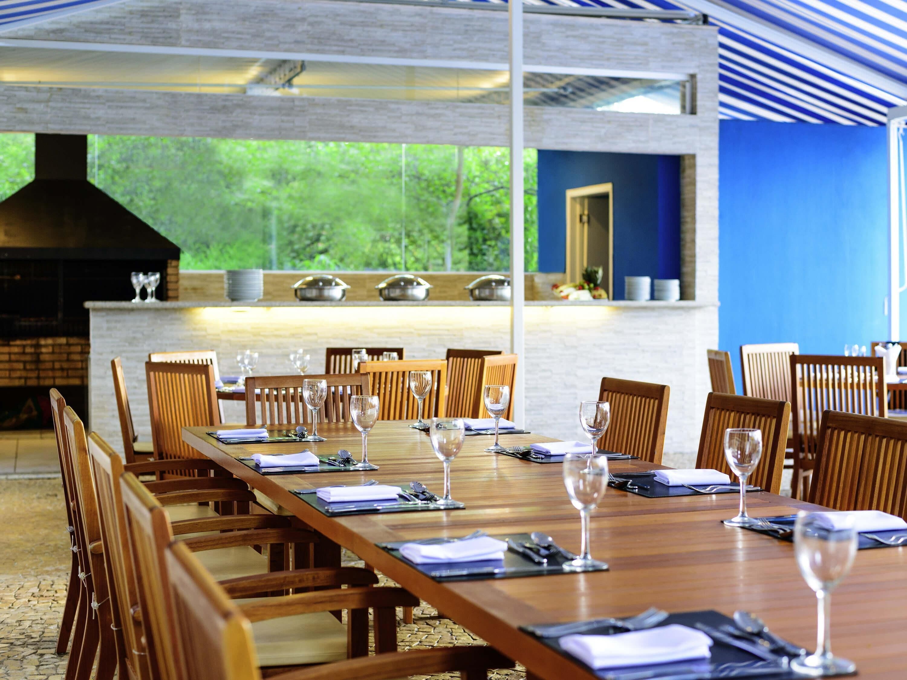 A long wooden dining table set with chairs, a grill, and a view of greenery outside.