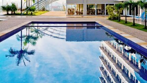 Een modern hotel met een zwembad, palmbomen en een heldere lucht.