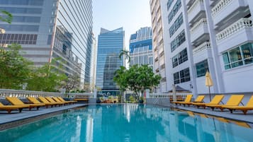 A swimming pool with sun loungers, surrounded by modern buildings.