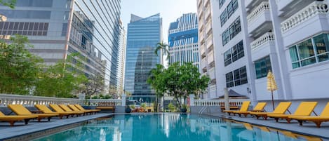 Una piscina con tumbonas, rodeada de edificios modernos.