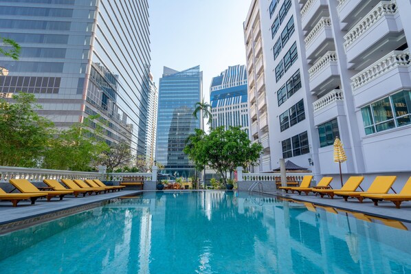 Une piscine entourée de bâtiments modernes, avec des chaises longues pour se détendre au soleil.