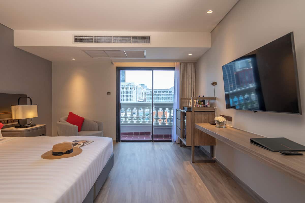 Une chambre d’hôtel équipée d’un lit, d’un bureau, d’une télévision et offrant une vue sur la ville grâce à une grande fenêtre.