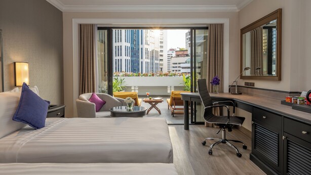 Une chambre d’hôtel comprenant un lit, un bureau, une chaise, une petite table et un balcon agrémenté de plantes et offrant une vue sur la ville.