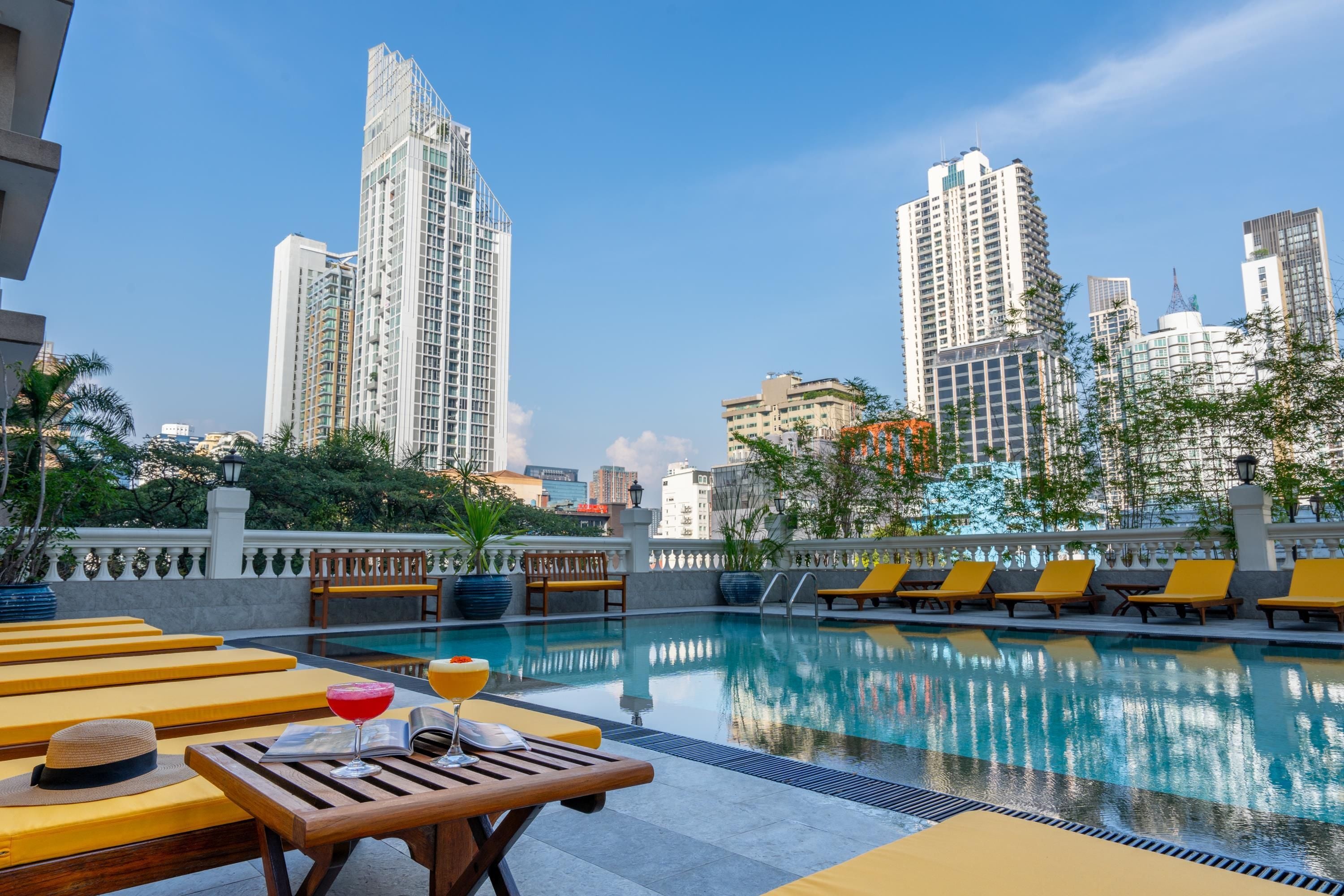 Un espace piscine aménagé sur le toit, avec des chaises longues et une table où sont servis des boissons, le tout entouré d’immeubles de la ville.