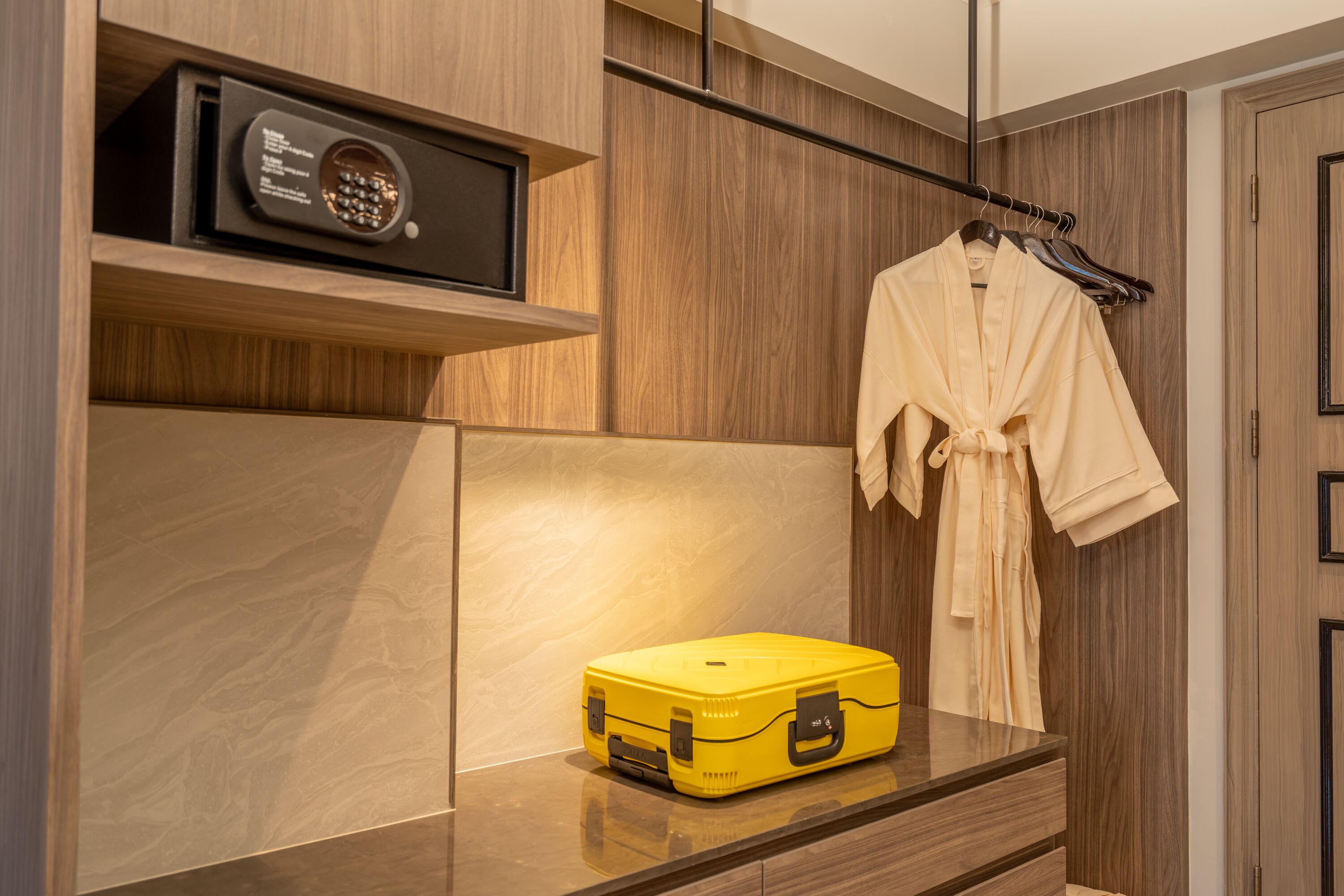 A modern bathroom with a wooden vanity, a yellow suitcase, and a robe hanging on a rack.