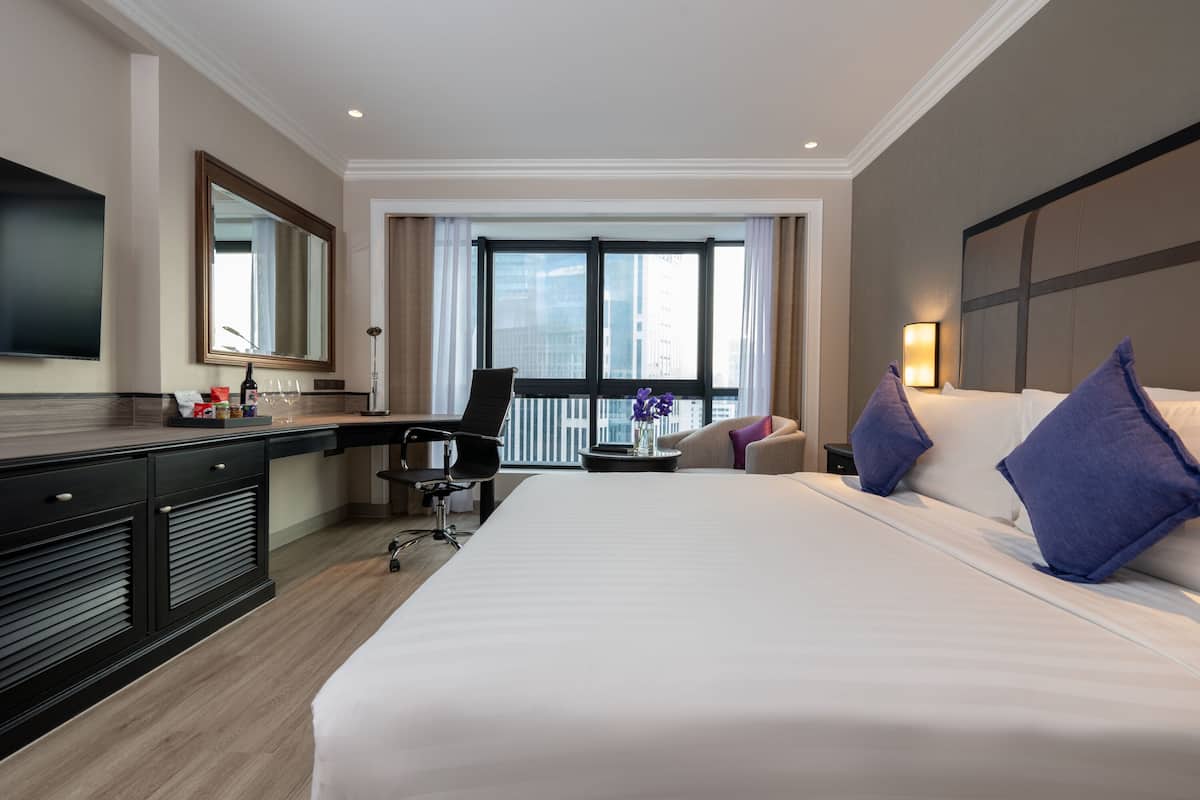 Une chambre d’hôtel avec un grand lit, un bureau, une chaise, une télévision et une fenêtre donnant sur la ville.