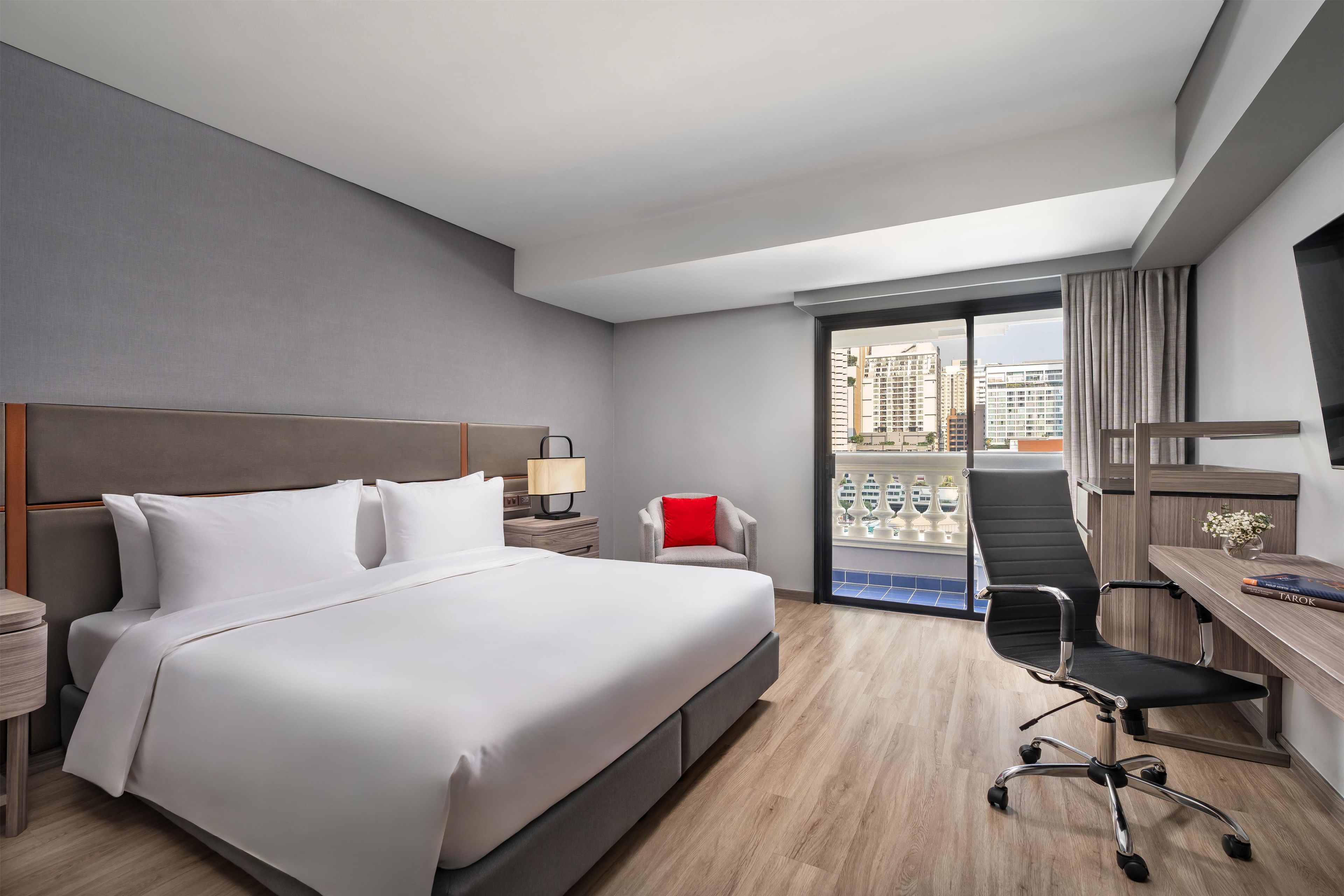 Habitación de hotel con una cama grande, un escritorio, una silla, una mesita de noche y vistas a la ciudad desde la ventana.