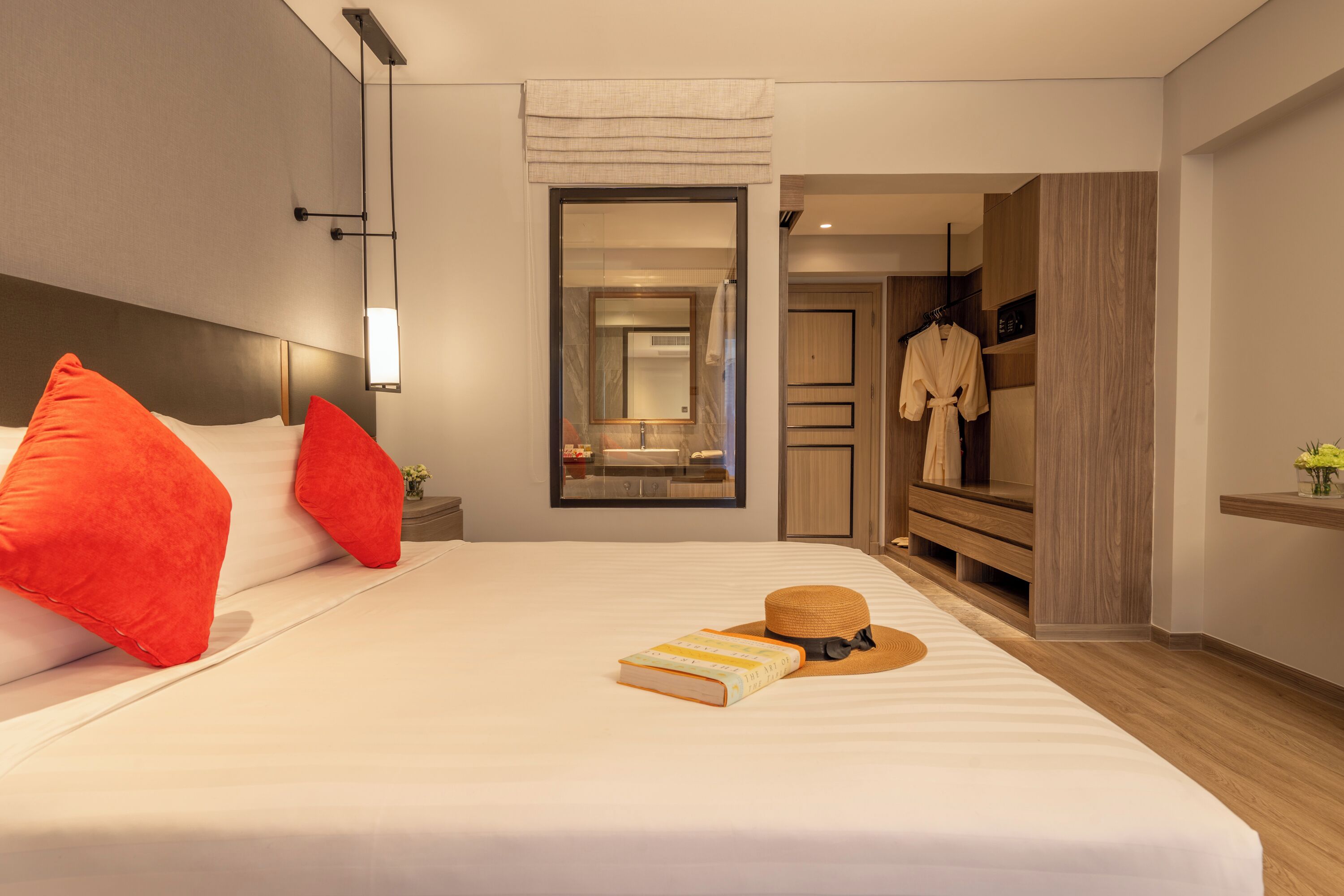 A modern hotel room with a large bed, a mirror, a robe, and a vanity area.