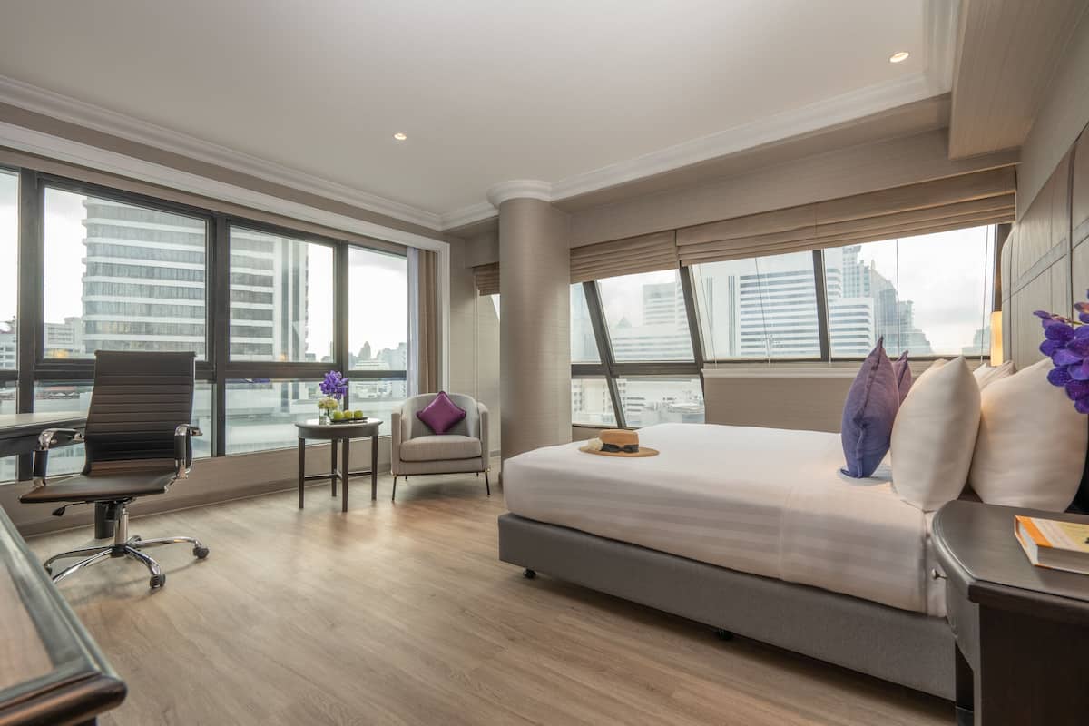Une chambre d’hôtel moderne dotée d’un grand lit, d’un bureau, d’une chaise et offrant une vue sur la ville grâce à de grandes fenêtres.