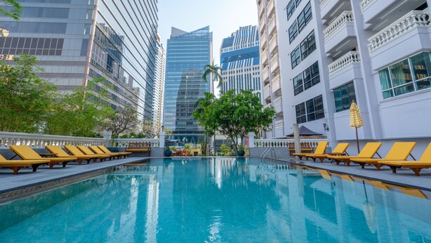 Una piscina con tumbonas, rodeada de edificios altos y vegetación.