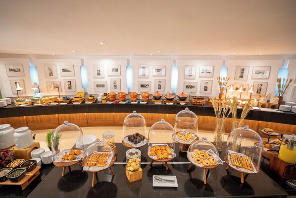 A buffet setup with various food items under glass domes, a wooden counter, and framed pictures on the wall. - NH Bangkok Sukhumvit Boulevard (Bangkok)
