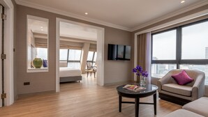 Una habitación de hotel moderna con un ventanal grande, un televisor de pantalla plana, un sofá, una silla y una mesita con un jarrón de flores.