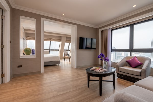 Una habitación de hotel moderna con un ventanal grande, un televisor de pantalla plana, un sofá, una silla y una mesita con un jarrón de flores.