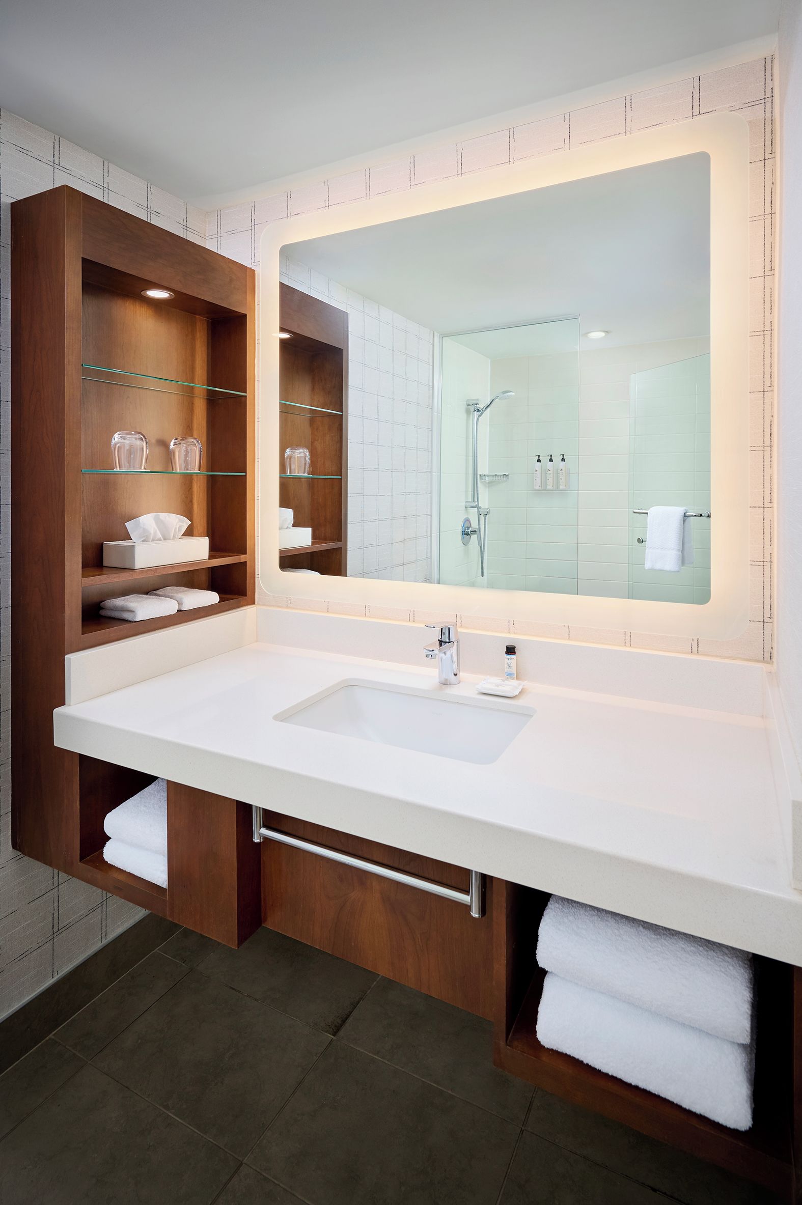 A modern bathroom with a large mirror, wooden vanity, and a shower area.