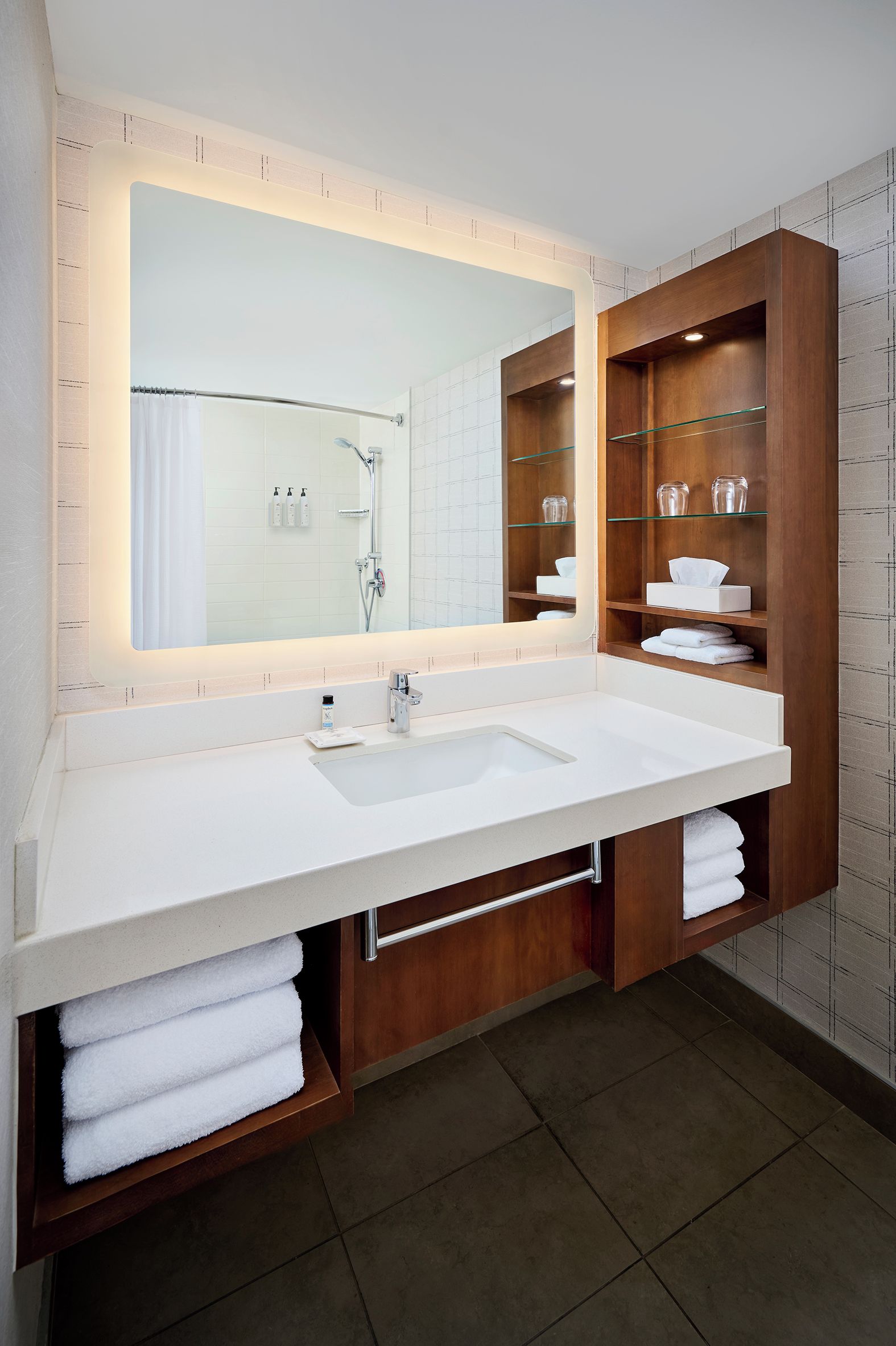Ein modernes Badezimmer mit großem Spiegel, weißem Waschbecken und Holz-Badmöbeln mit Glastablagen.