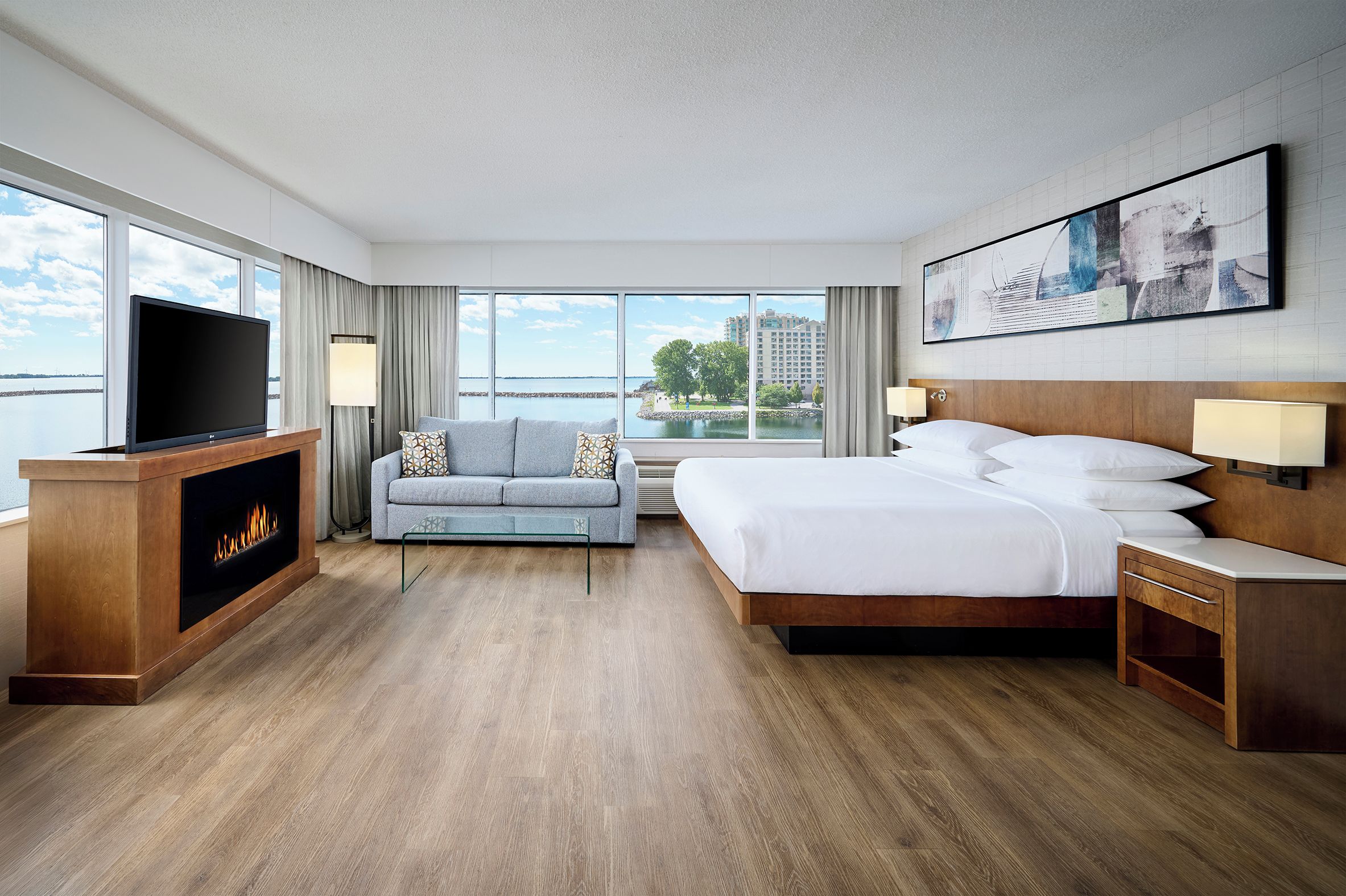A hotel room with a bed, a sofa, a TV, a fireplace, and large windows with a view.