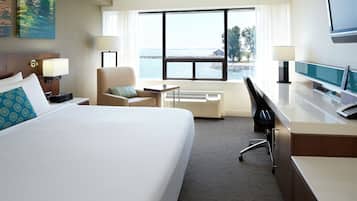 Quarto de hotel com uma cama grande, uma escrivaninha, uma cadeira, uma TV e uma janela com vista para a água.
