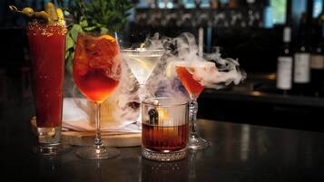 Tre cocktail su un bancone del bar, con sullo sfondo sfocato bottiglie e una pianta.