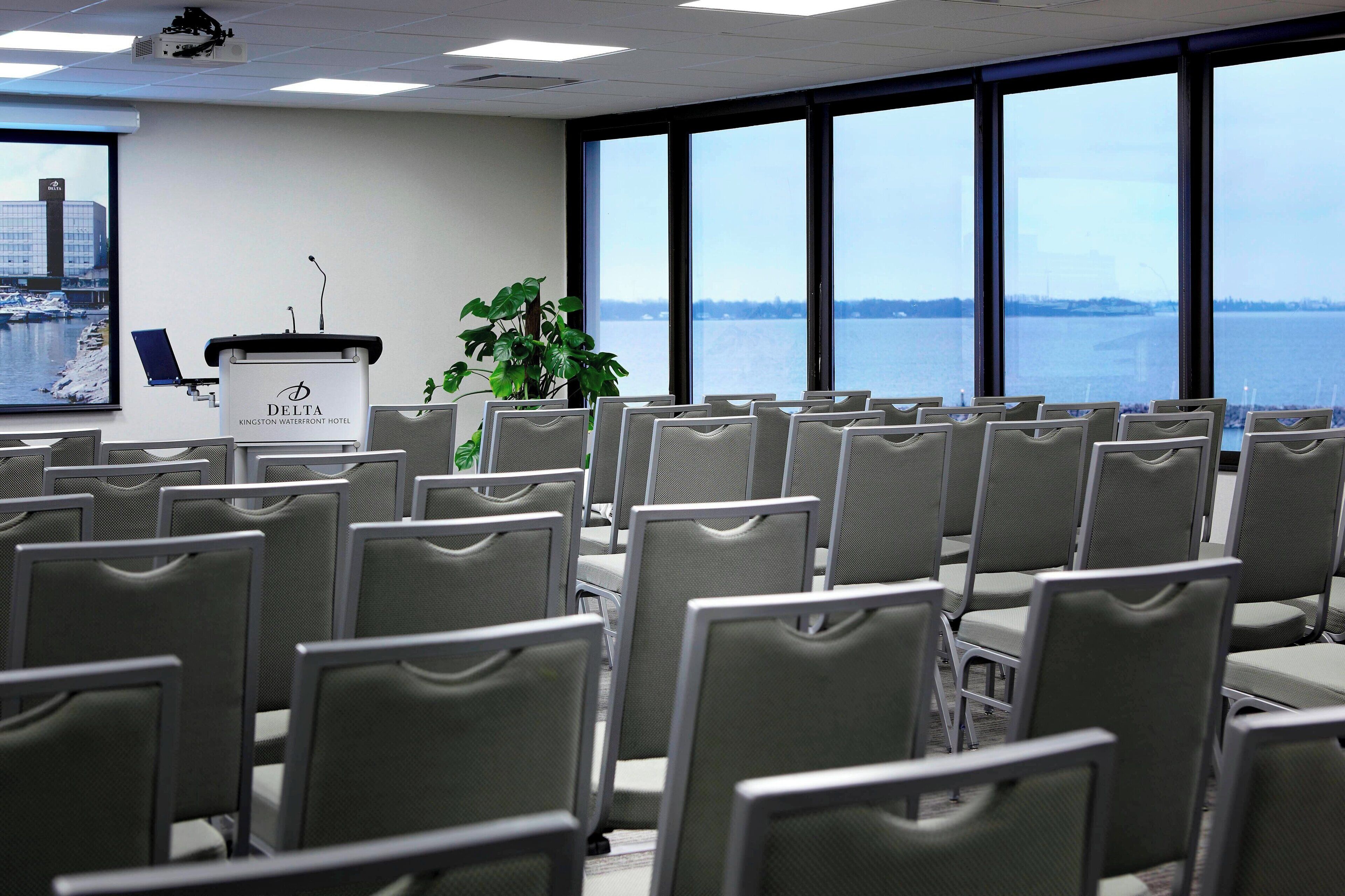 Un salón de conferencias con filas de sillas, un atril con el logo de Delta y un ventanal con vista a un cuerpo de agua.