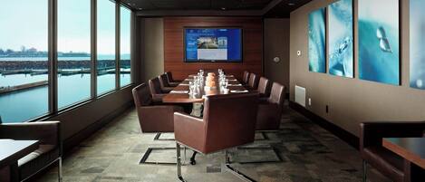 A conference room with a large table, chairs, a screen, and a view of a body of water.