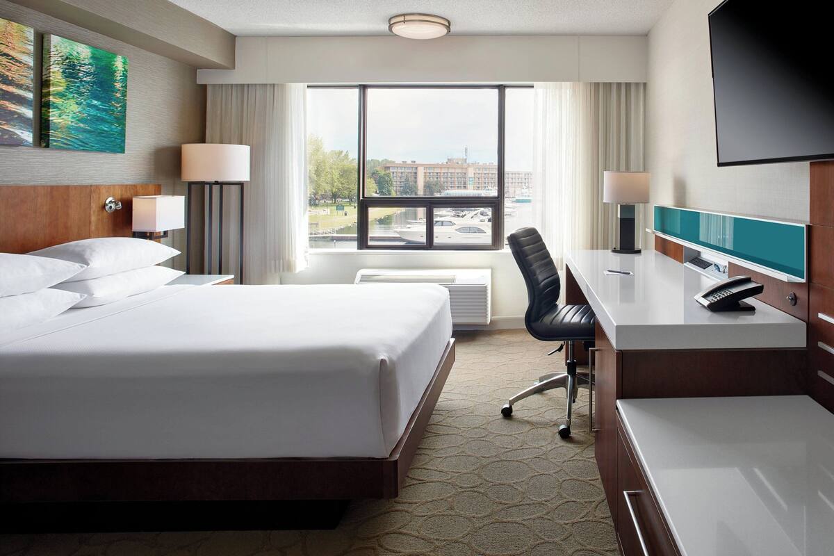 A hotel room with a large bed, a desk with a computer, a chair, and a TV.
