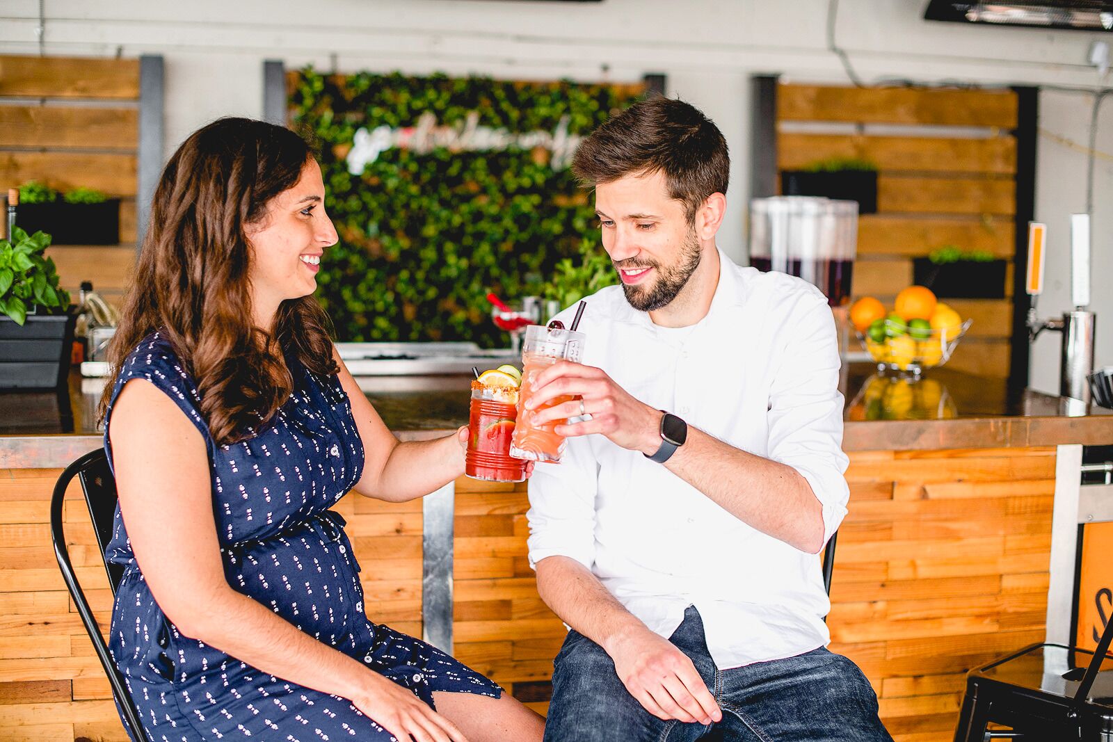 Two people seated at a wooden table in a modern kitchen with a green wall and a fruit bowl in the background.
