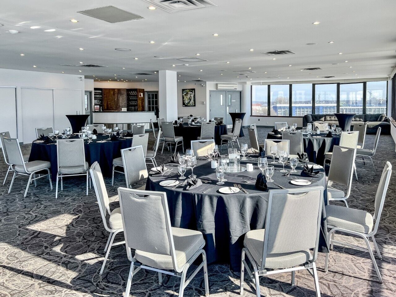 Sala de conferências com mesas redondas, cadeiras e um espaço bar.
