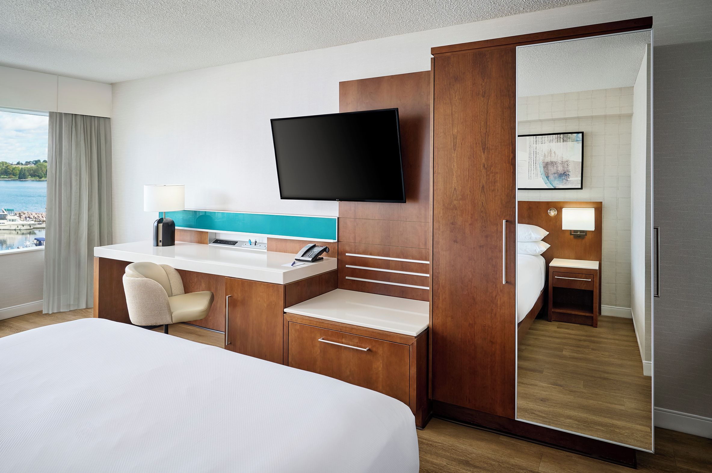 Habitación de hotel con cama, escritorio con computadora, televisor de pantalla plana, espejo y vistas al exterior.
