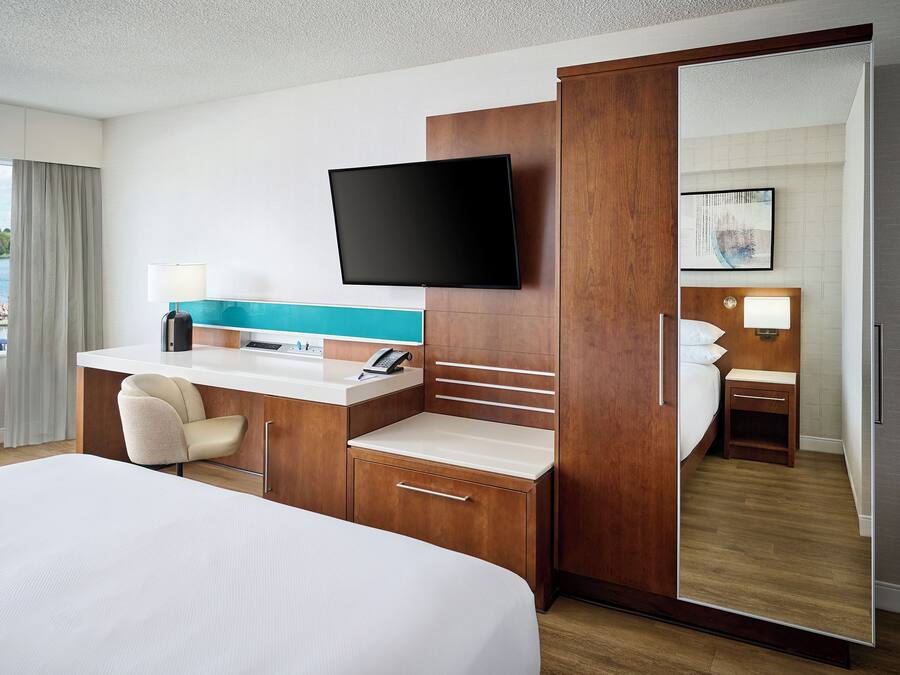 Habitación de hotel con cama, escritorio con computadora, televisor de pantalla plana, espejo y vistas al exterior.
