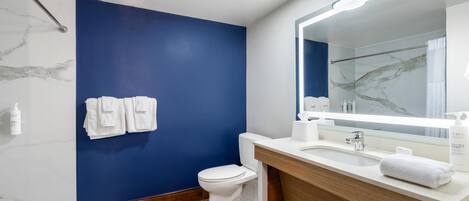 A modern bathroom with a blue accent wall, a white toilet, a wooden vanity, and a large mirror.