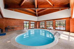 Una piscina interior con techo de madera, paredes de ladrillo y ventanas grandes.