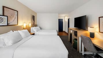 A hotel room with two beds, a desk with a chair, a television, and artwork on the walls.