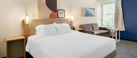 A hotel room with a large bed, a desk, a chair, a window with curtains, and artwork on the walls.