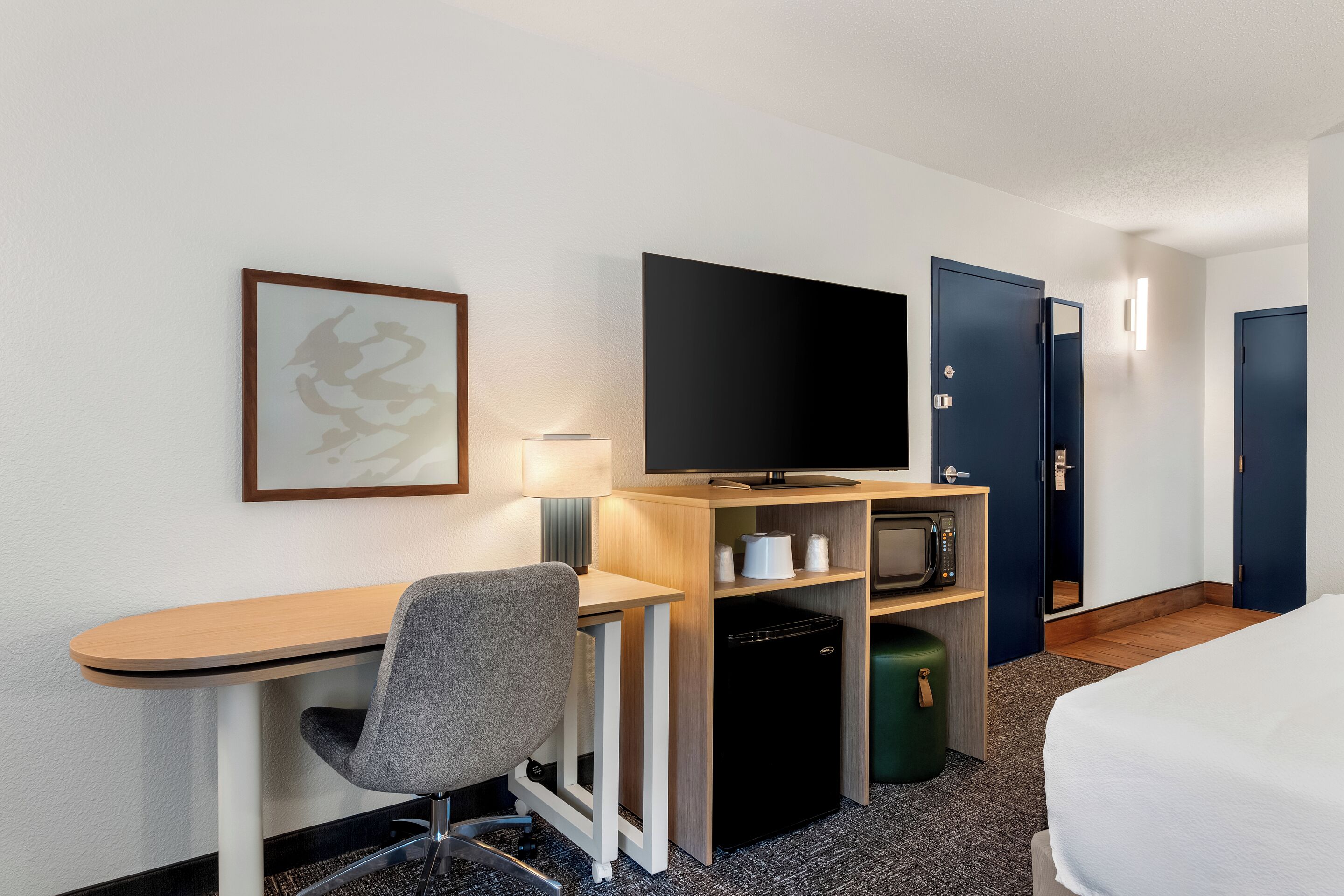 A hotel room with a desk, chair, television, microwave, and a bed.