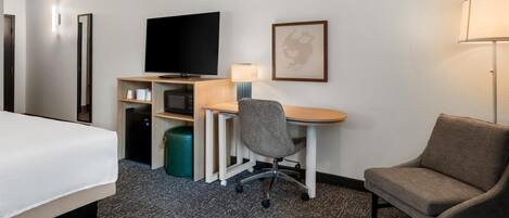 Une chambre d’hôtel comprenant un lit, un bureau avec un ordinateur, une chaise, une télévision et une lampe.