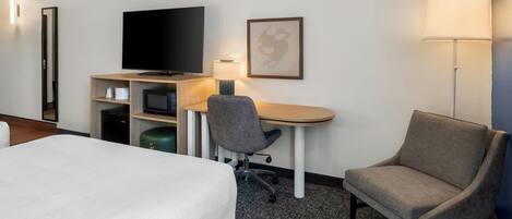 A hotel room with a bed, a desk with a chair, a television, a lamp, and a framed picture on the wall.