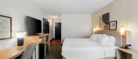 A hotel room with a bed, desk, chair, television, and a door leading to another room.