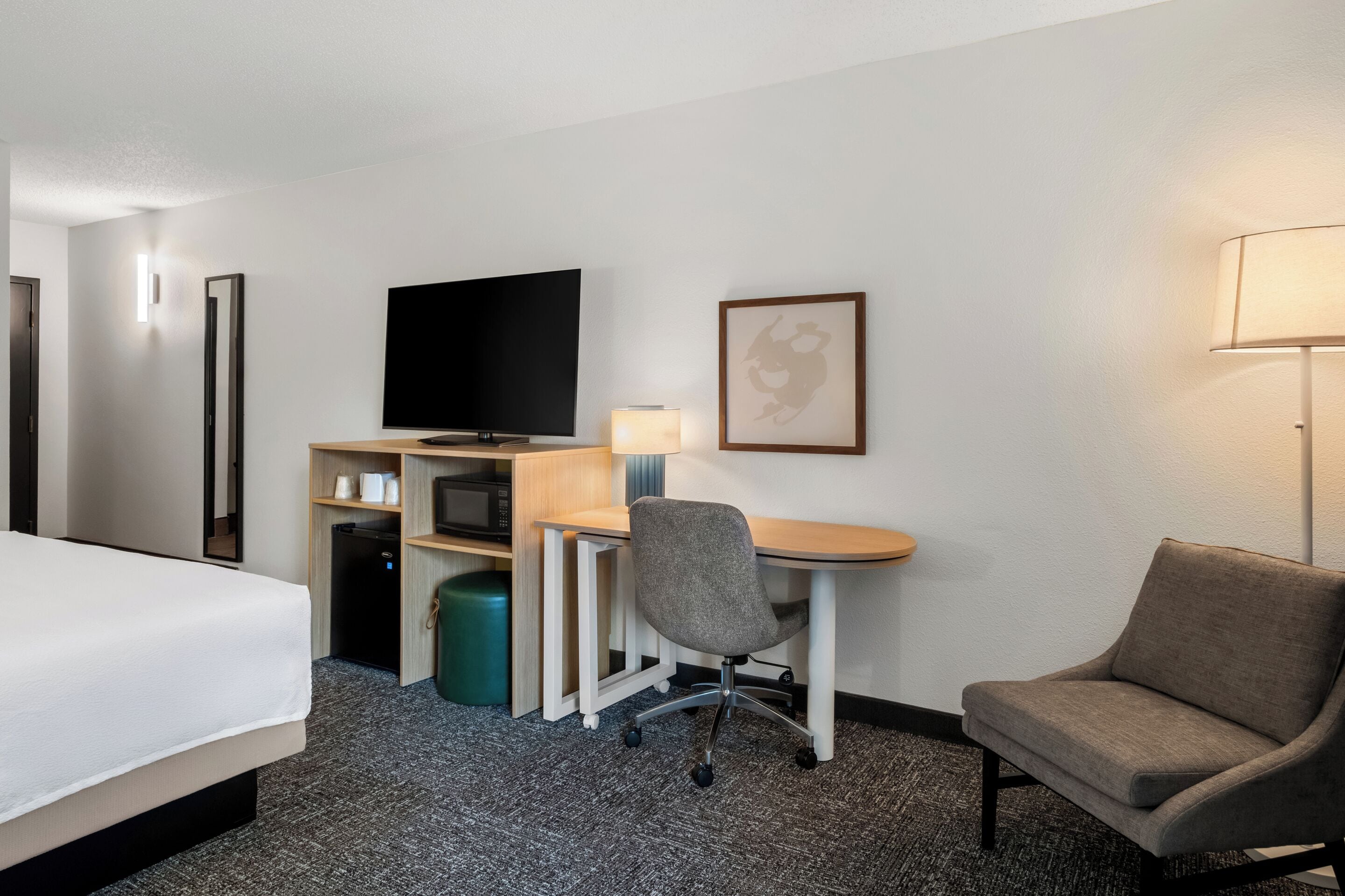 Habitación de hotel con cama, escritorio, silla, televisor y lámpara.