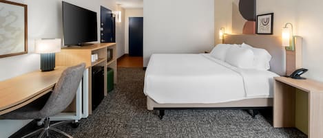 A hotel room with a bed, desk, chair, television, and a small kitchenette.