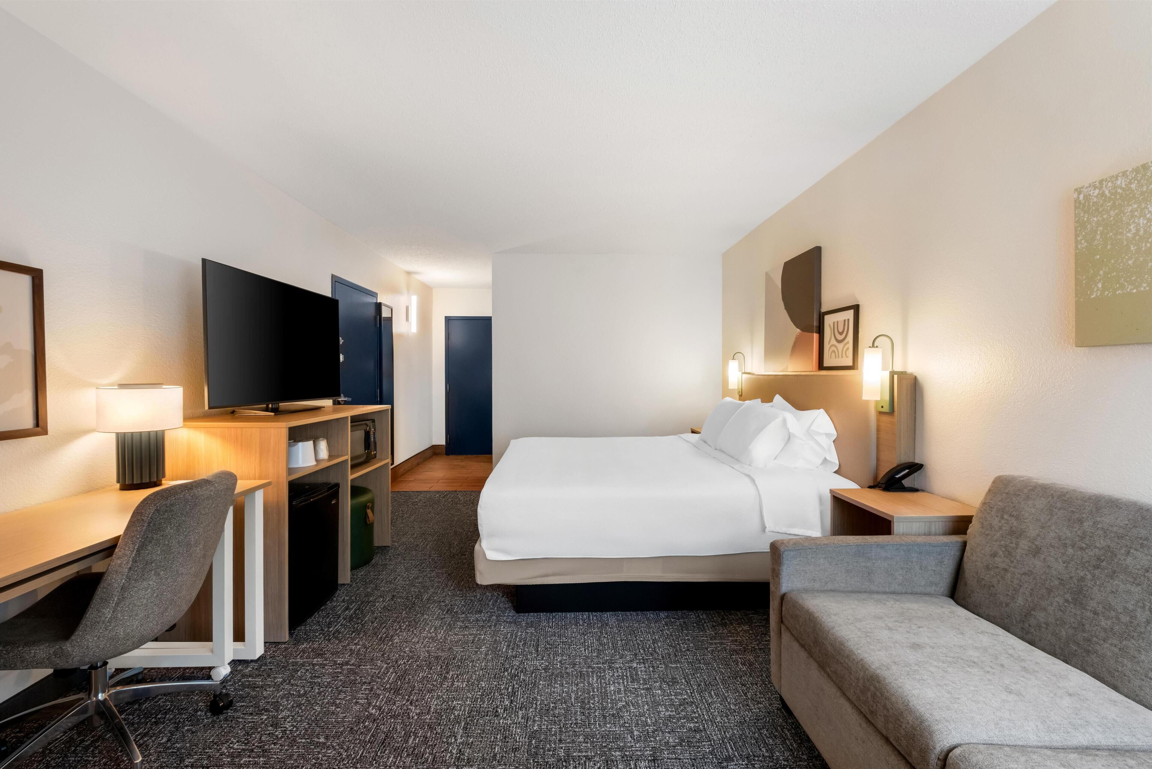 A hotel room with a bed, a desk, a chair, a television, and a sofa.
