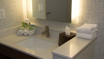 A hotel bathroom with a sink, mirror, towel dispenser, and toiletries.